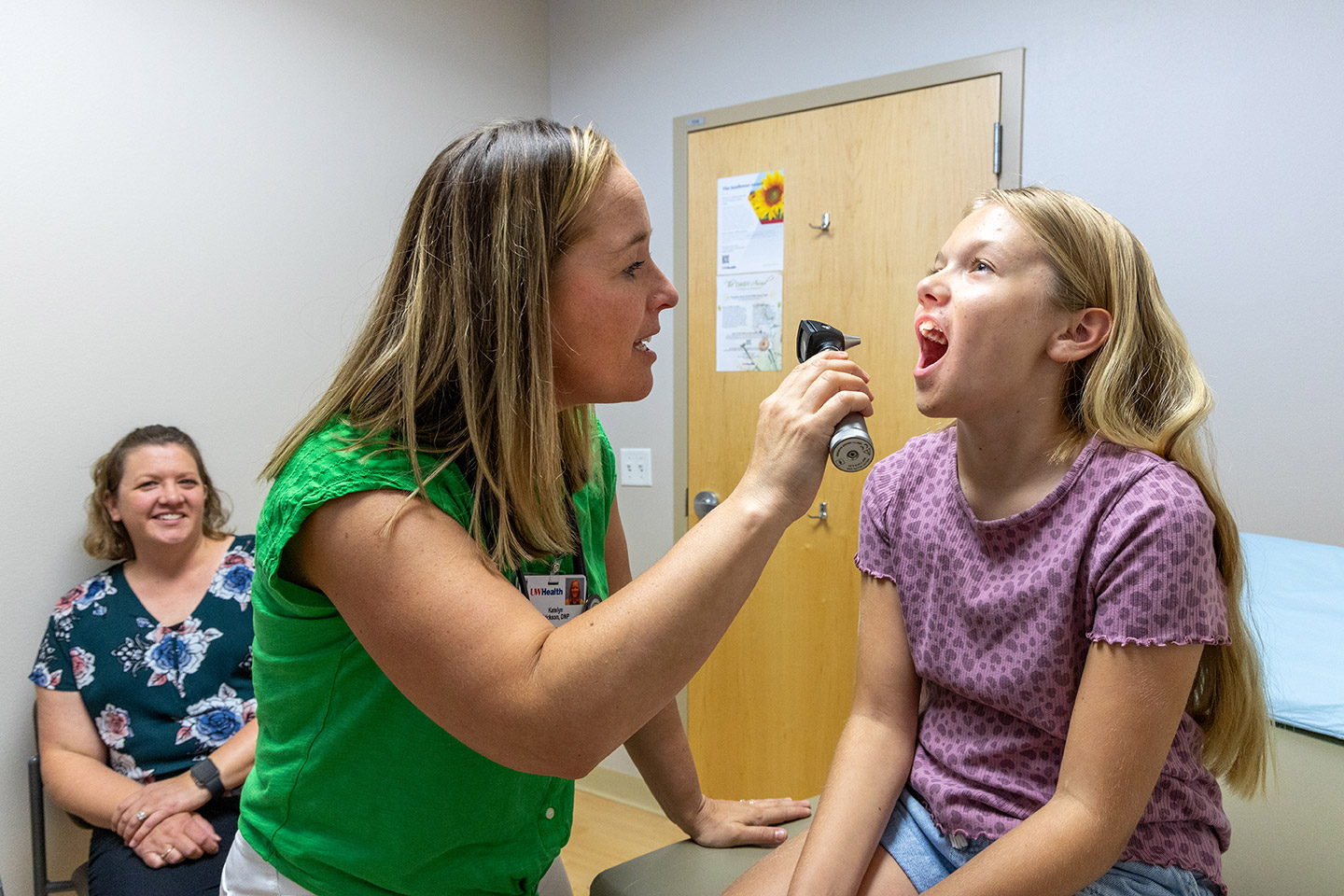 A family doctor sees a patient in a clinic, using an otoscope to check a young girl's mouth.