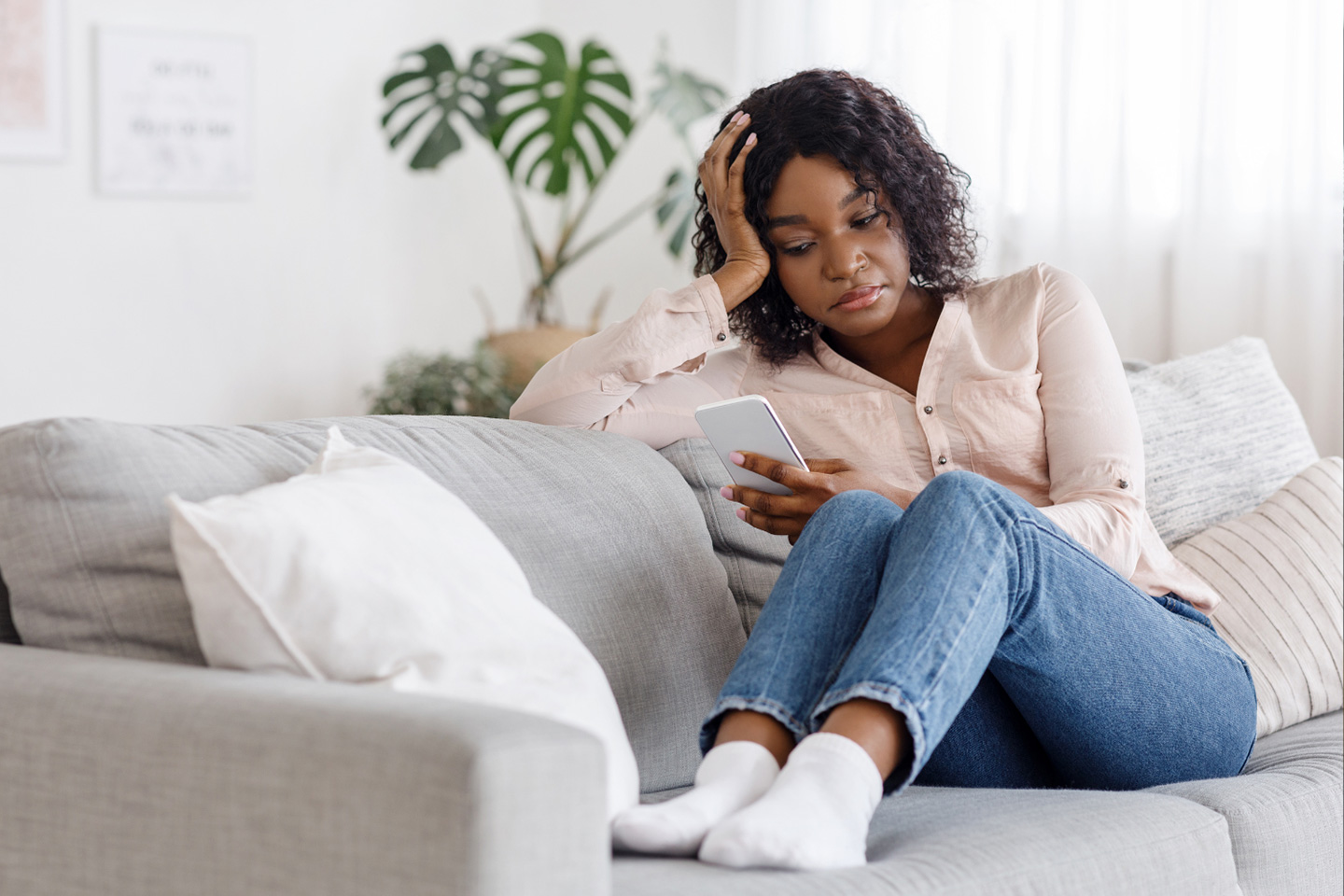 African American female looks at phone while sitting on couch. 