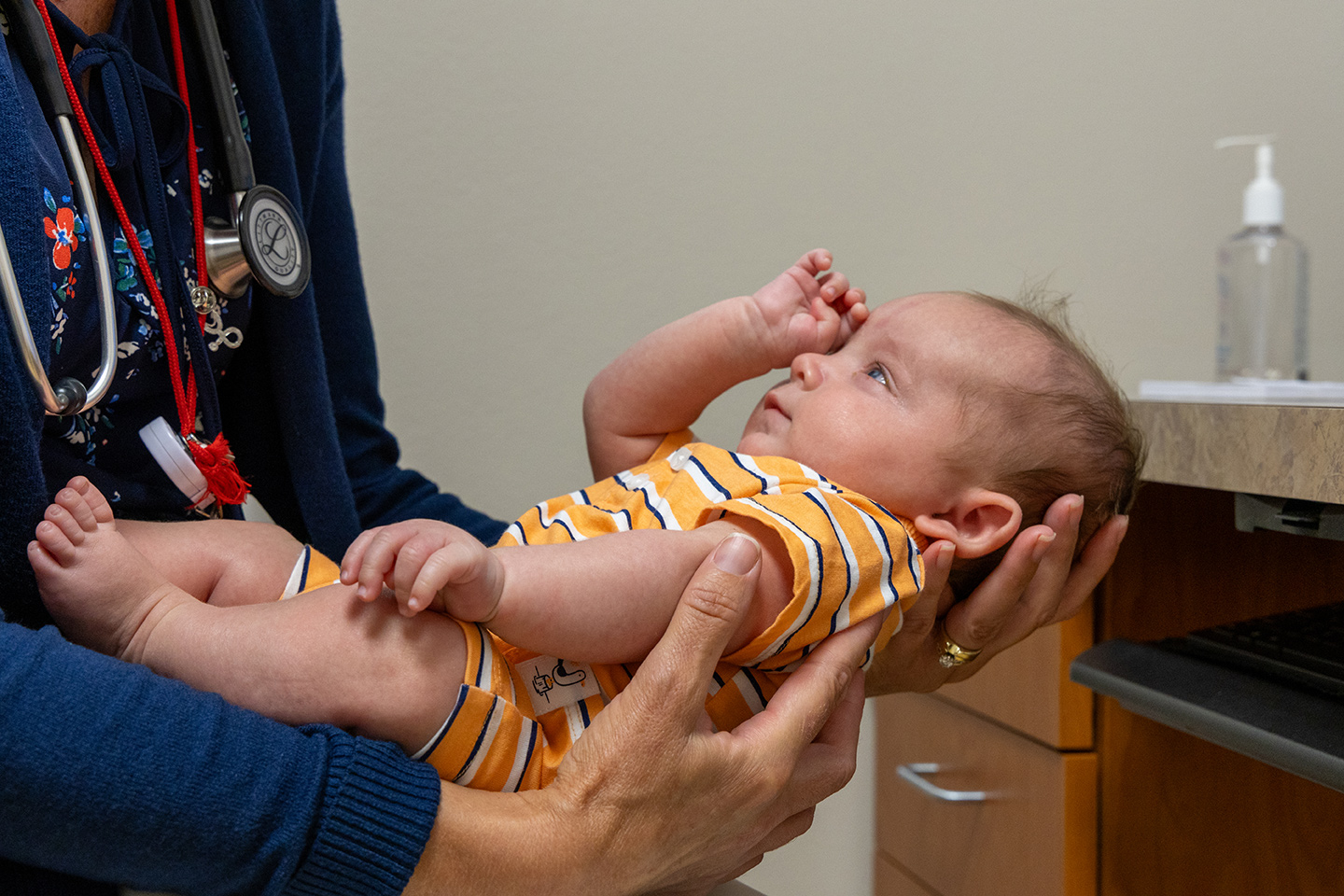 Female doctor cradles baby in her hands in a clinical setting.