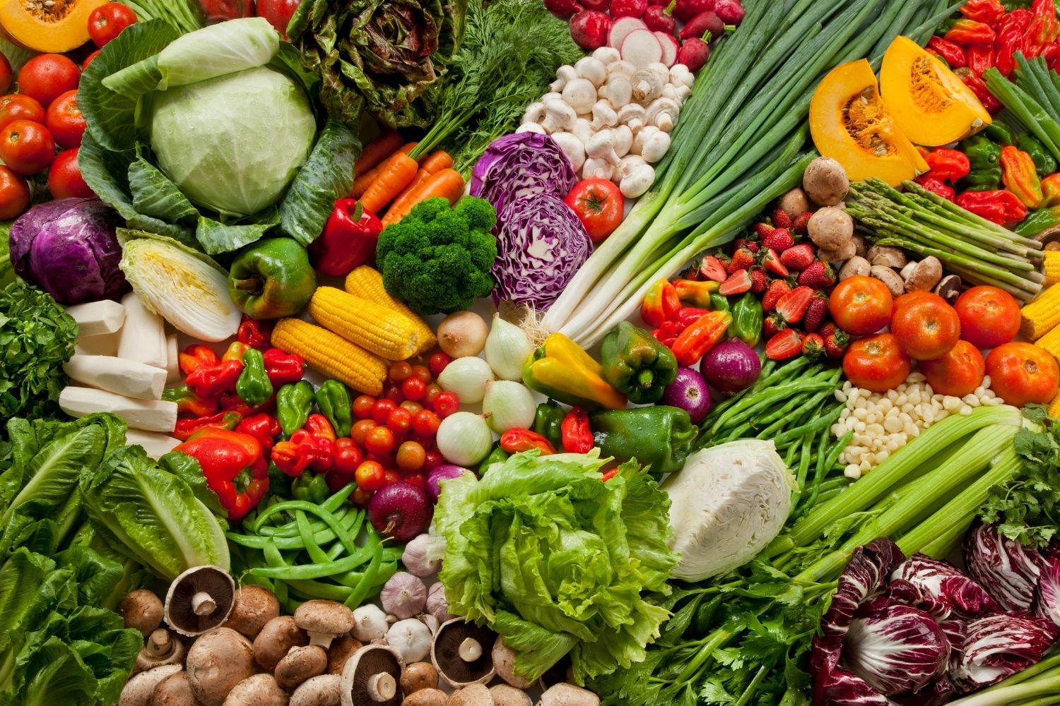 Colorful composition of assorted vegetables: bell tomatoes, lettuce, onions, peppers, strawberries, broccoli, corn, and mushrooms among others.