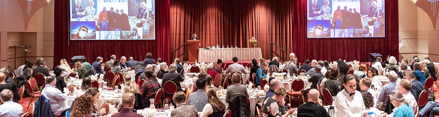 Wide shot of Renner-Hansen attendees seated at tables, dining, while facing the podium for presentations.