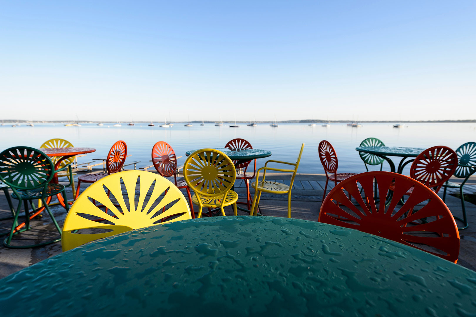 Morning dew covers Memorial Union Terrace chairs and tables at the University of Wisconsin-Madison as Lake Mendota provides a calm background during an autumn sunrise.