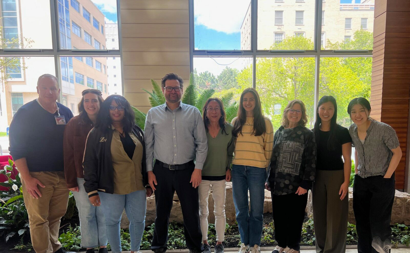 Group photo of Implementation Science and Engineering Lab team members standing indoors near large windows.