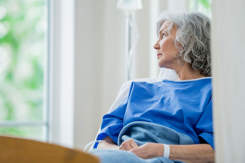 An elderly Caucasian woman is alone looking out a window.
