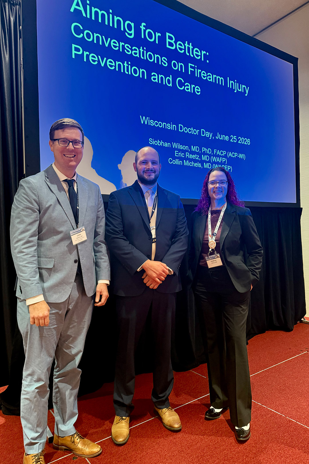 Doctors stand in front of screen with presentations title displayed.