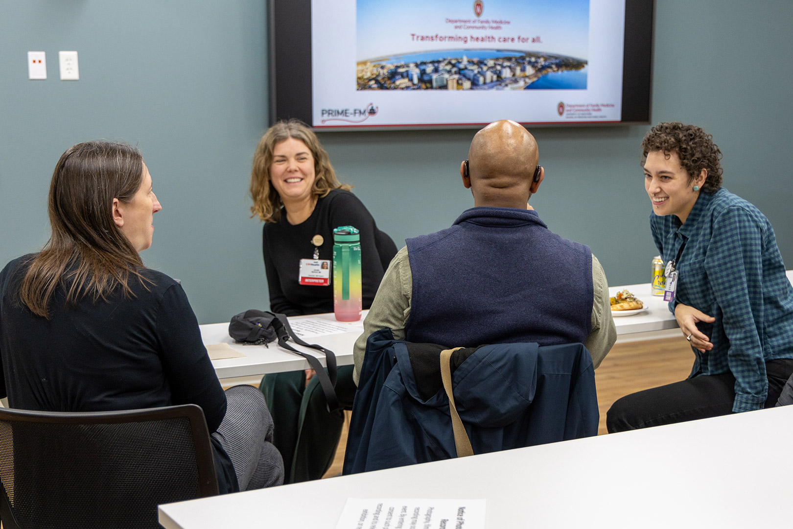 Medical students and colleagues chat and laugh around a table.  
