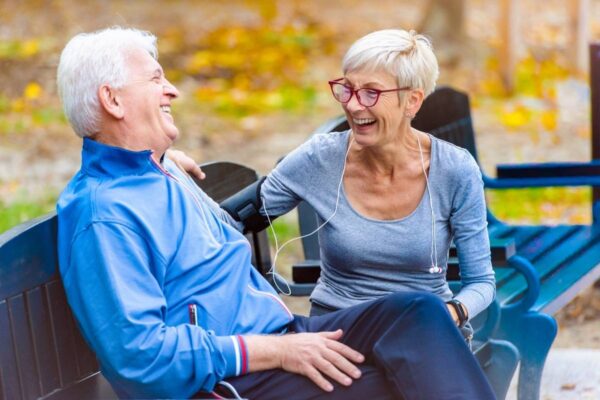 A senior man and woman have a conversation on a park bench before a morning walk.