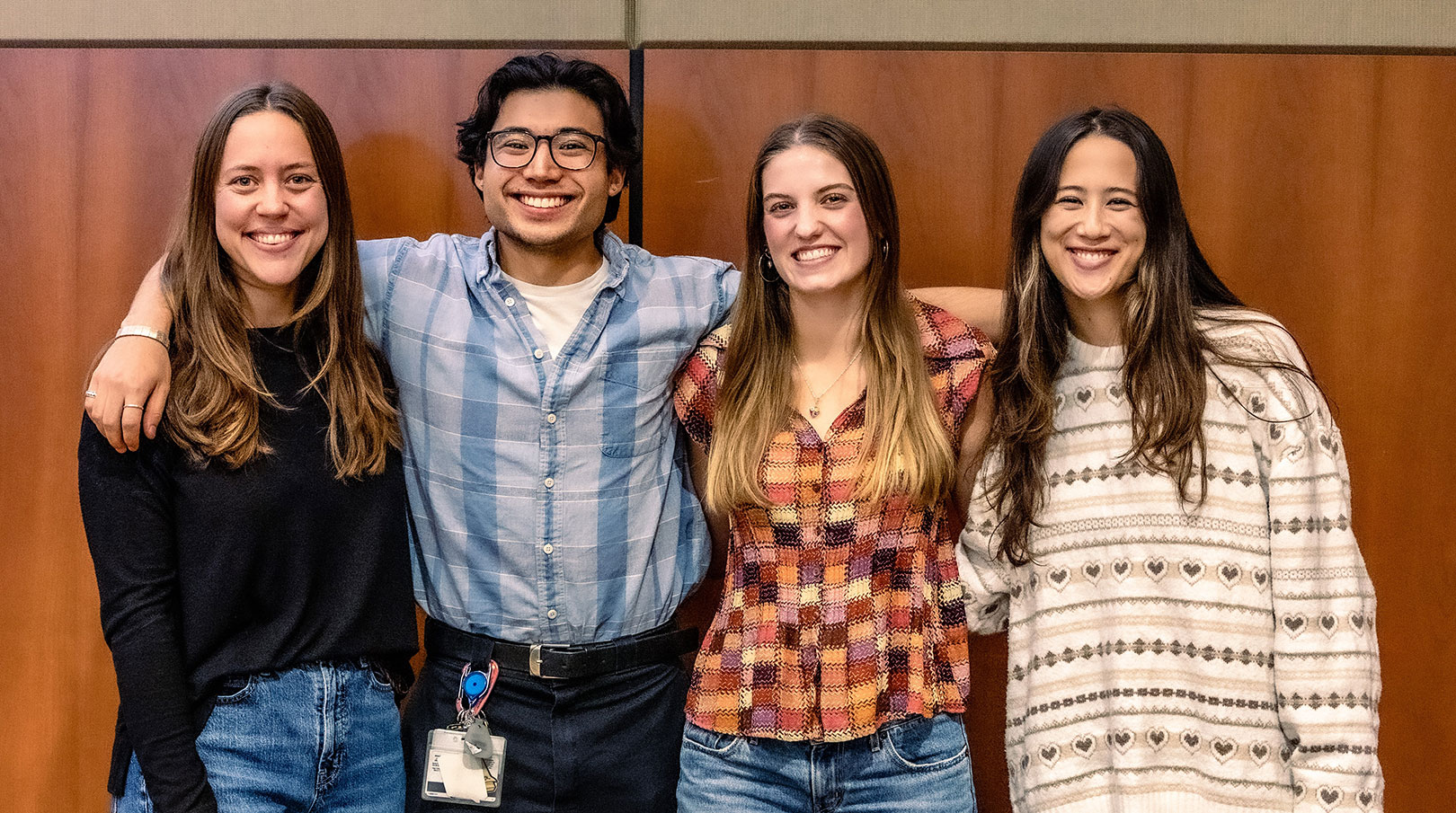 Four medical students stand arm in arm against a wood panel background.