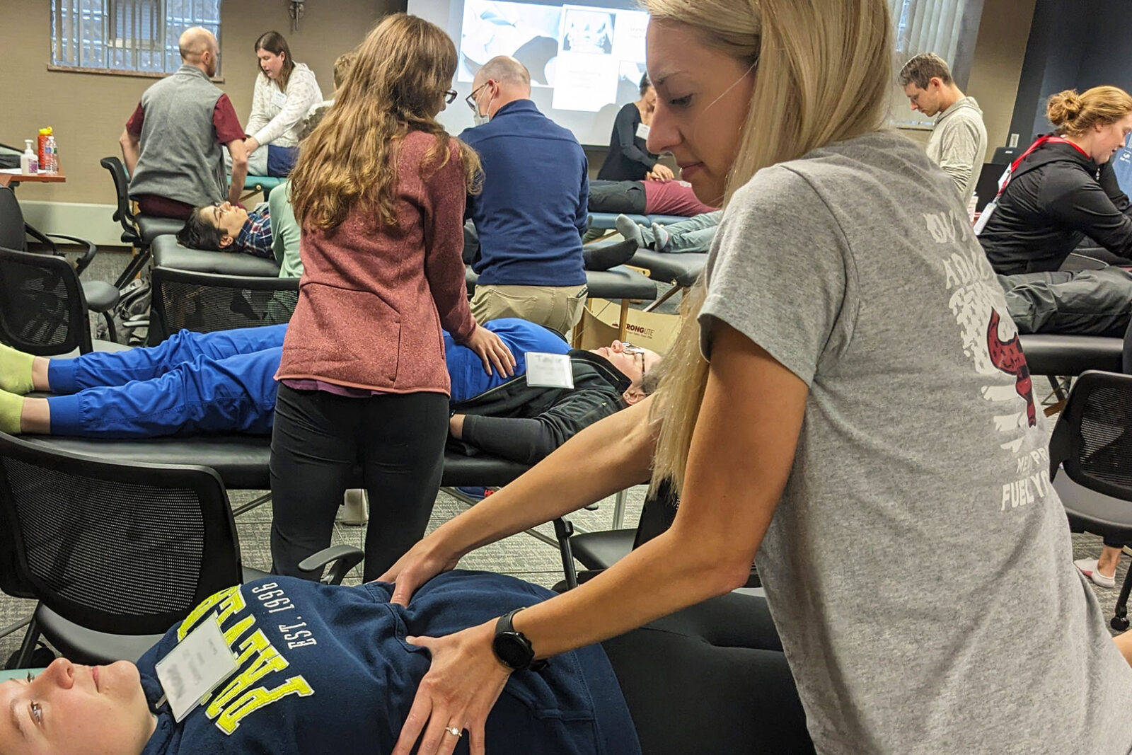 A room filled with osteopathic residents and faculty practicing OMT. 