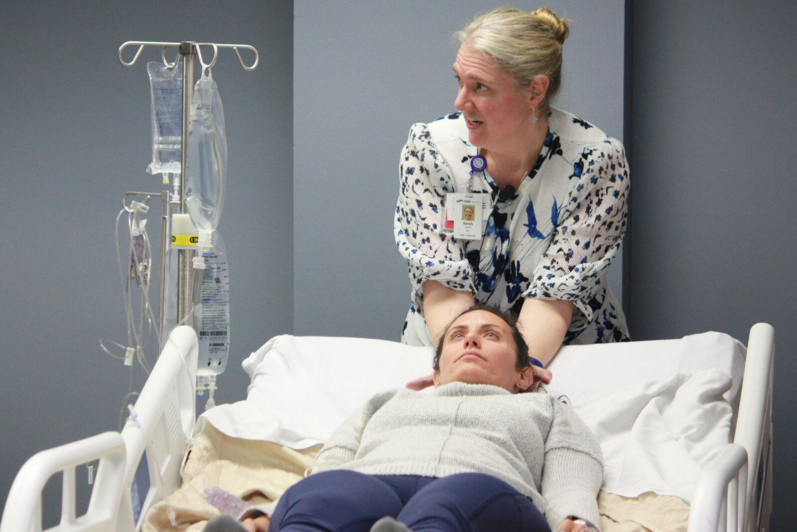 A faculty member demonstrates a technique on a resident acting as a patient in a hospital bed.
